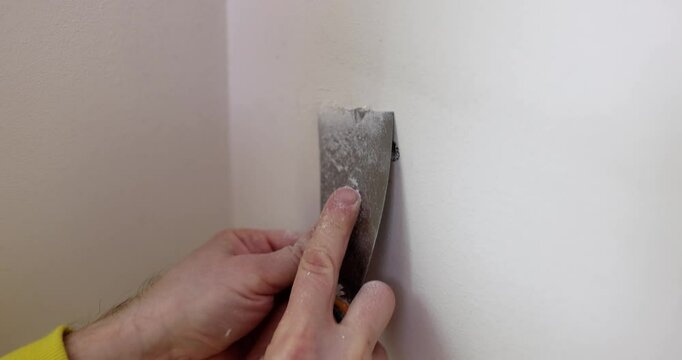 Male worker grinds surface of white wall with holes from removed screws. Builder processes panel with putty knife. Repairing works in house