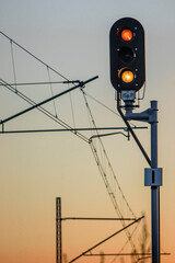 Glowing railway semaphore, against the background of electric traction for trains. Sunset on a warm day.  Vertical Staff. repeating semaphore