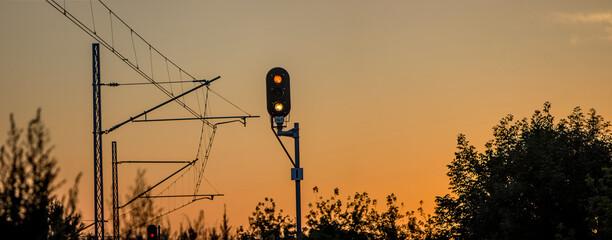 Glowing railway semaphore, against the background of electric traction for trains. Sunset on a warm day. Repeating semaphore. Panorama 