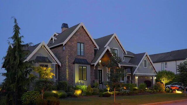Establishing shot of two story stucco luxury house with garage door, big tree and nice landscape at night in Vancouver, Canada, North America. Night time on June 2024. ProRes 422 HQ.