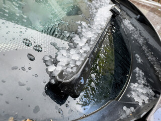 Close-up of a car windshield covered in hailstones and raindrops, highlighting the aftermath of a hailstorm with ice pellets accumulated around the windshield wiper