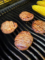 Burgers on the grill with corn on the cob.