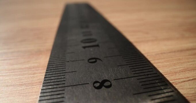 Metal ruler with digits and lines for measuring length on wooden table. Repairer of premises tool on desk in room. Manual foreman instruments
