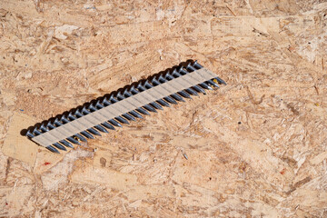 Construction background, collated nail gun nails, connected with paper tape; on a sheet of oriented...