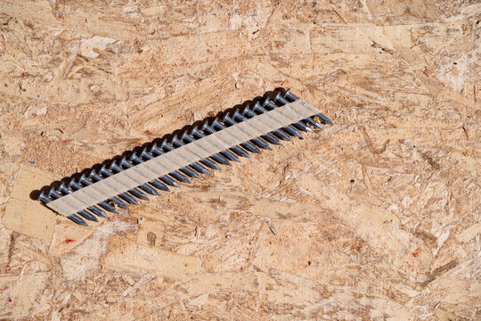 Construction background, collated nail gun nails, connected with paper tape; on a sheet of oriented strand board, OSP, wood supplies
