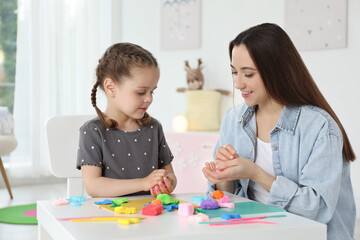 Fototapeta premium Smiling mother and her daughter sculpting with play dough at table indoors