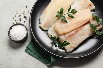 Plate with raw cod fish, spices and parsley on light table, flat lay