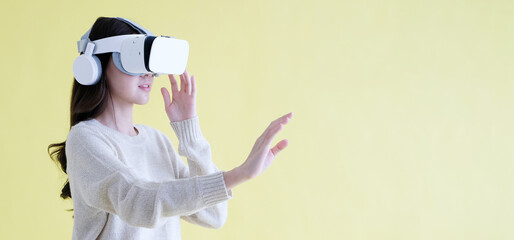 Asian woman wearing virtual reality, VR headset and trying to touch something with hand while stand...
