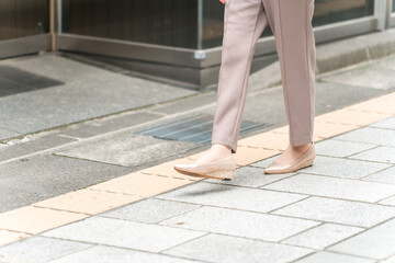 街を歩くビジネスウーマンの足元（点字ブロック・視覚障害者）
