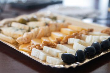 Una sofisticada tabla de quesos, perfectamente preparada para una experiencia culinaria exquisita. La imagen presenta una variedad de quesos finos, junto a olivas negras dando un toque mediterráneo