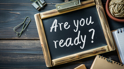 Chalkboard with question "Are you ready?" and notebooks on table. Preparing for exam