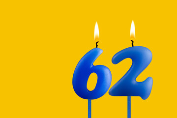 Blue birthday candle on yellow background - Number 62