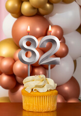 Cupcake with birthday candle on balloons background - Number 82