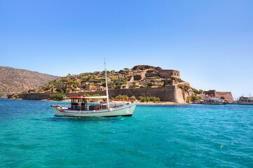 A white touristic boat in turquoise water of the Gulf of Elounda in front of Spinalonga island, north-eastern Crete, in the municipality of Agios Nikolaos