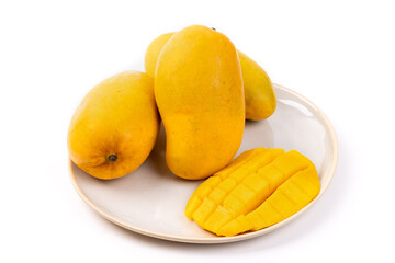 Three yellow Ataulfo mangos on a plate with half a mango cut into cubes isolated on white