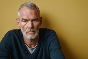 Portrait of a senior man with grey beard and mustache in blue sweater on yellow background