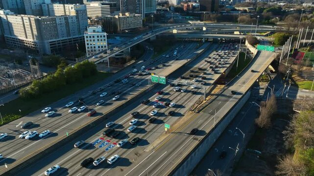 Cars leaving busy interstate highway of american town at sunrise. Downtown buildings and homes with bridge in USA. Atlanta City in Georgia. Aerial top down shot.
