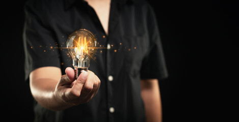 Hand holding a lighting bulb with lighting against a black background.