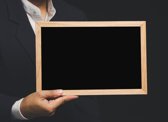 Businessman holding blank chalkboard while standing on a black background.