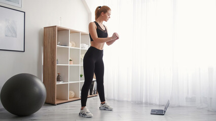 Video workout. Fitness motivation. Strong muscles. Weight loss training. Fit woman in activewear working out looking at laptop light room interior free space.