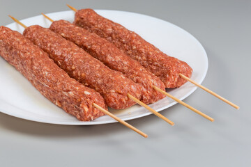 Raw lula kebab on wooden skewers on dish, close-up