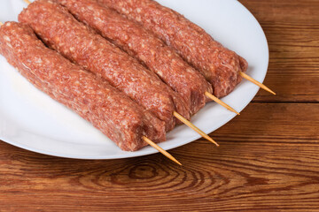 Raw lula kebab on skewers on dish on rustic table
