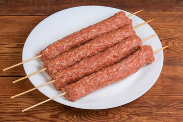 Raw lula kebab on skewers on dish on rustic table