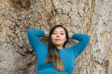 Woman seated leaning against a tree with pensive attitude.