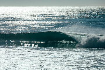 Perfect hollow glassy surfing wave breaking along the shore on a bright sunny morning