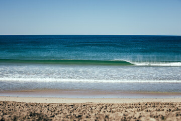 Tranquil view of a clear blue ocean with a small wave breaking in the foreground captured from the sandy shoreline