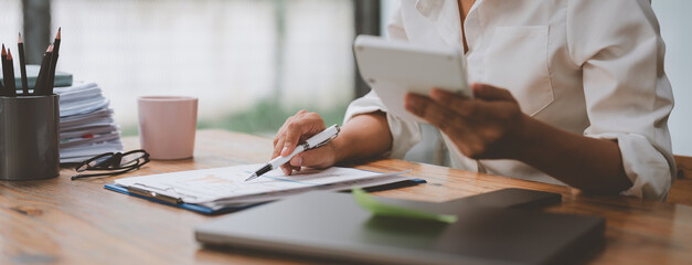 Confident businesswoman working with laptop in office Female office worker uses a calculator to...