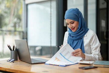 Modern office Muslim businesswoman wearing hijab sits with laptop online, doing paperwork Sitting and working on financial projects, analysis, calculations, startup business ideas, e-commerce, online.