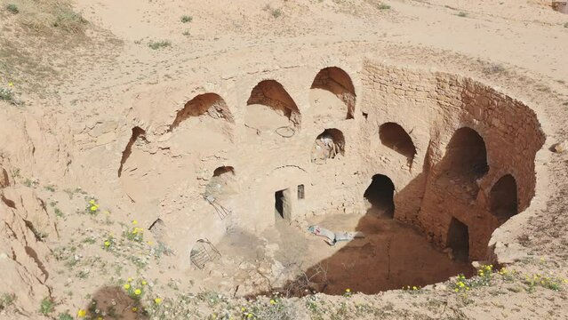 Abandoned Berber dwellings with arched doorways carved into walls of earthen pit in Matmata, Tunisia, revealing history of ancient troglodyte architecture