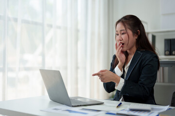 Surprised and happy businesswoman shows joyful expression after viewing news results, business approval results and financial approval results on laptop at office. Startup business growth concept.