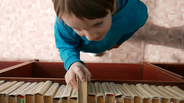 Close-up of a boy taking a book from a book case