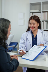 Fototapeta premium Confident Asian female doctor explains and questions a retired female patient attending a private clinic for treatment and therapy. Health concept, health insurance.