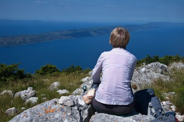 Naklejka premium Senior woman sitting on mountain peak with beautiful view on Adriatic sea
