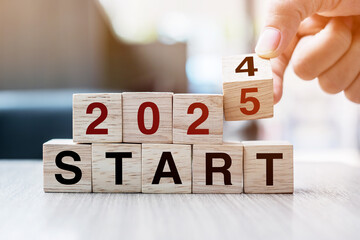 Businessman hand holding wooden cube with flip over block 2024 to 2025 Plans word on table...