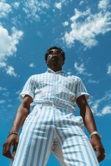 Blue Sunny Sky. African American Man in Trendy White and Blue Striped Summer Clothes under Clear Blue Sky