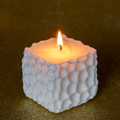 Square handmade candle on golden background.