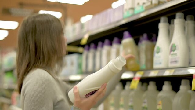 A woman selecting a bottle of laundry detergent from a supermarket shelf, focusing on household cleaning products. High quality 4k footage