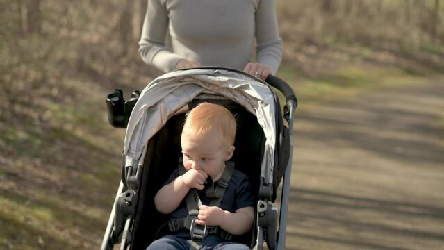 A mother pushing a baby in a stroller along a park path, enjoying a peaceful walk on a sunny day, highlighting outdoor activities and family time. High quality 4k footage