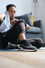 Sporty man sits and looks at smartwatch while wiping sweats after doing exercise at home