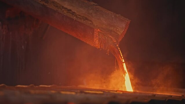 Streams of hot metal fill molds at factory. Stock footage. Beautiful molten metal pours into molds. Streams of metal flow at metallurgical plant
