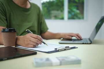 A householder manages household expenses while working at a desk, tracking various costs such as...