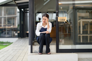 Asian female coffee shop owner Stressed barista Headache and regret hanging the shop closed sign on the entrance. I feel sad that I had to close my business. business shut down startup business idea.