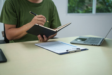 A householder manages household expenses while working at a desk, tracking various costs such as...