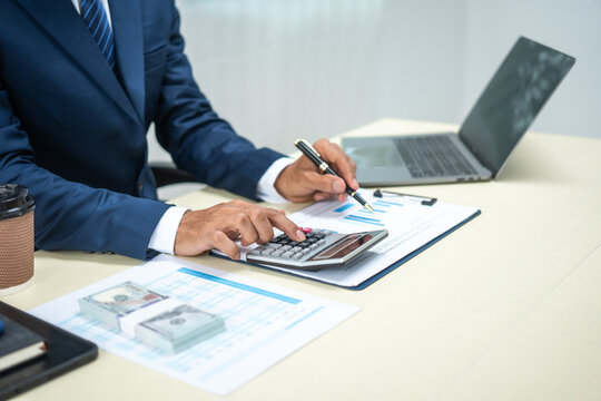 A banker in a suit works at a desk handling loans, analyzing client financial data, providing financial advice, dealing with stocks and the stock market, and studying economic situations.