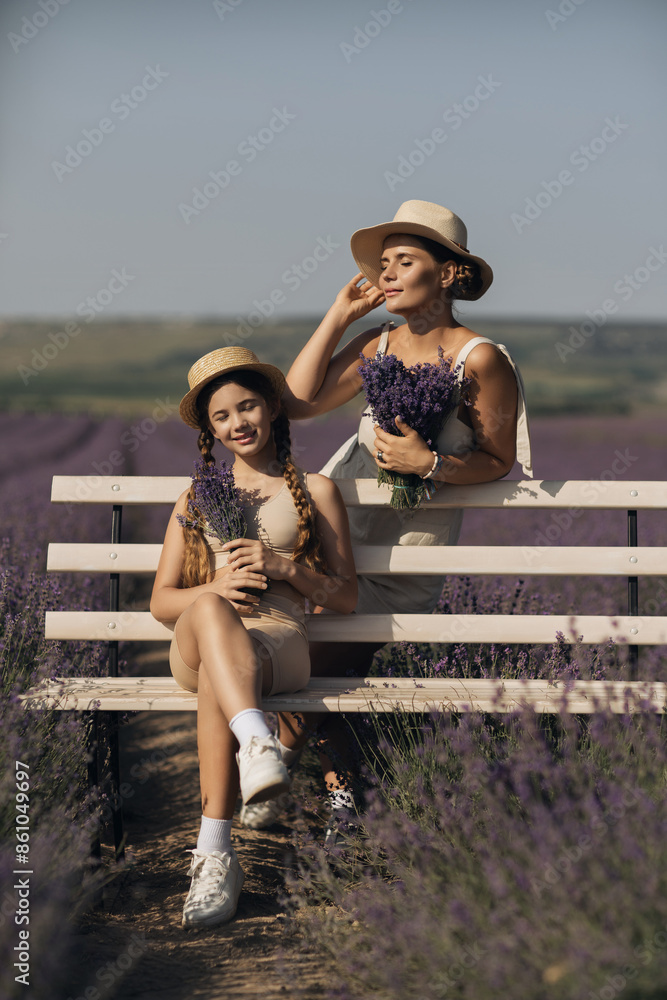 Wall mural woman child sitting bench in field lavender. The woman is holding a bouquet of flowers, and the child is holding a bouquet as well. The scene is peaceful and serene.