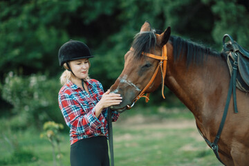 Obraz premium Happy blonde with horse in forest. Woman and a horse walking through the field during the day. Dressed in a plaid shirt and black leggings.